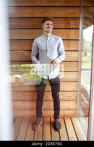 Smiling man holding digital tablet while standing at home Stock Photo