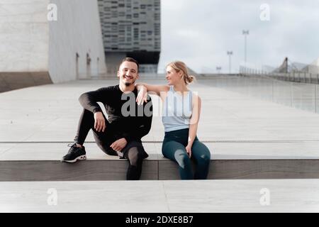 Couple smiling while sitting by retaining wall Stock Photo