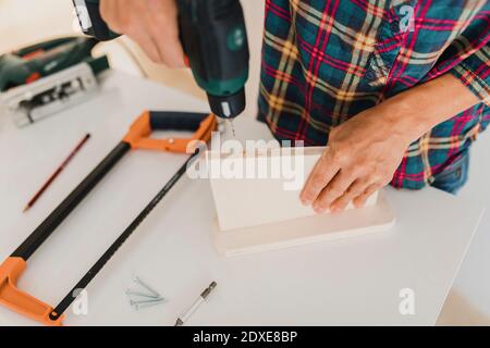 Woman using electric drill on wood while working at home Stock Photo
