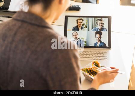 Businesswoman having lunch while attending video conference through laptop at office Stock Photo
