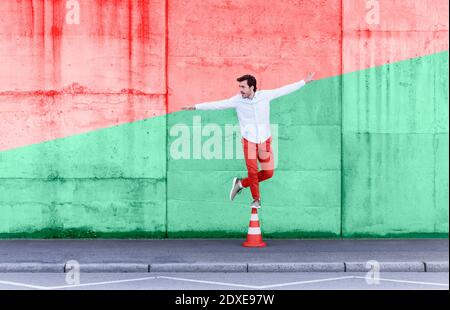 Carefree man standing on traffic cone against multi colored wall Stock Photo