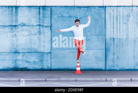 Man balancing while standing on traffic cone against blue wall Stock Photo