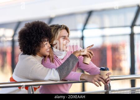 Smiling woman pointing to friend at railroad station Stock Photo