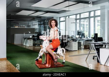 Excited businesswoman sitting on rocking horse at office Stock Photo