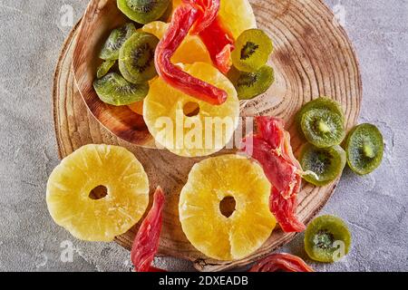 Dried fruits: Yellow candied pineapple rings, red papaya and green kiwi on a wooden board. Flat lay Stock Photo