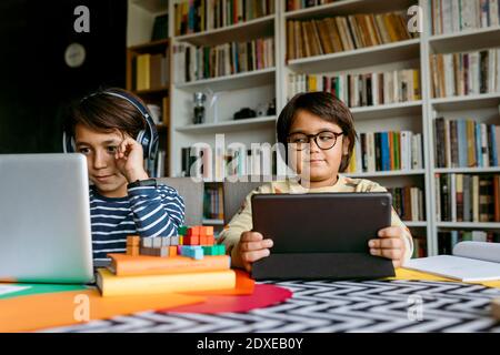 Smiling boy e-learning through laptop while male friend peeking at home Stock Photo