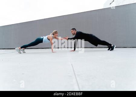 Young couple giving high-five while doing plank against wall Stock Photo