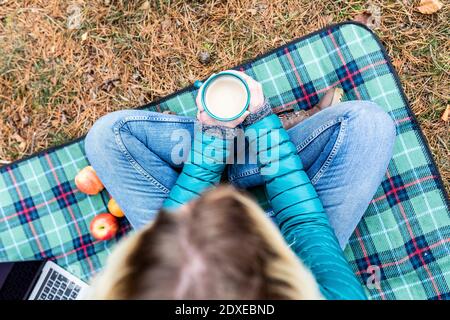 Woman holding tea cup while sitting on picnic blanket at remote location Stock Photo