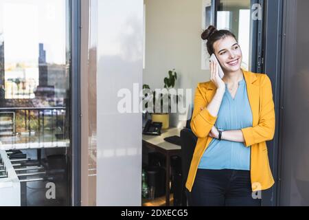 Businesswoman talking on mobile phone while standing at door in office Stock Photo