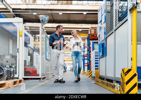 Female and male colleagues discussing while walking in factory Stock Photo