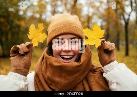 Cheerful young woman with autumn leafs in public park Stock Photo