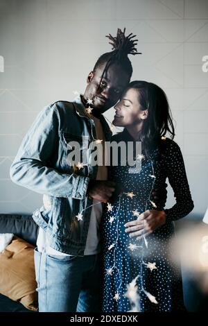 Young man and smiling pregnant woman with star shaped lights at home Stock Photo