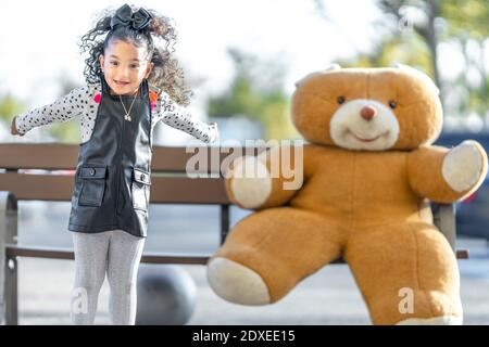 Playful girl jumping while playing with teddy bear on bench in background Stock Photo