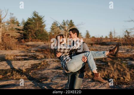Young man carrying girlfriend during autumn hike Stock Photo