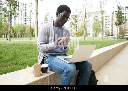 Businessman disinfecting hands while looking at laptop during coronavirus Stock Photo