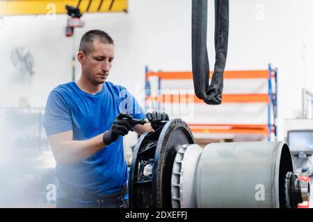 Male technician repairing machine while standing at illuminated factory Stock Photo