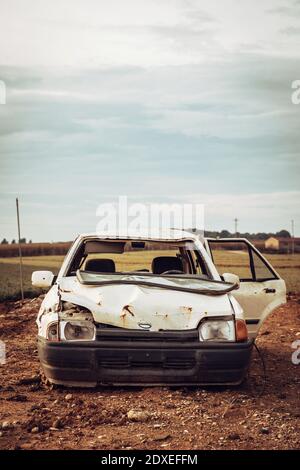 White wrecked car abandoned in middle of field Stock Photo