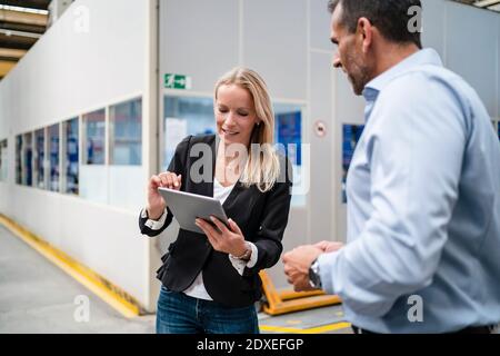 Female colleague using digital tablet while businessman standing beside her at factory Stock Photo