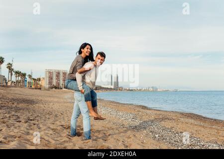 Young man giving piggyback ride to woman against sky at beach Stock Photo