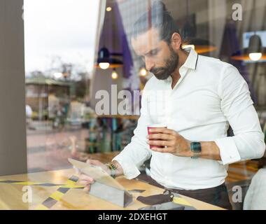 Candid portrait of bearded businessman drinking coffee in front of digital tablet inside cafe Stock Photo