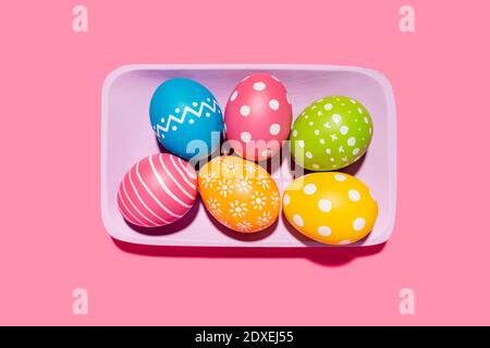 Handmade painted Easter eggs in purple tray on pink background Stock Photo