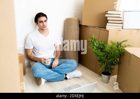 Thoughtful young man holding coffee cup while sitting in new house Stock Photo