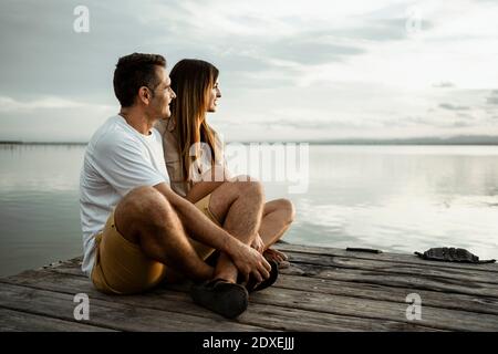 Relaxed mature couple looking away while sitting on jetty against sky Stock Photo