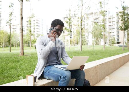 Businessman on phone using laptop while sitting with lunch in city Stock Photo