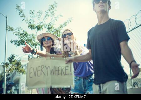Young friends hitchhiking while holding placard with written text Stock Photo
