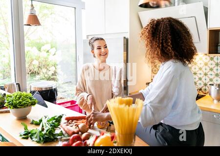Happy female coworkers cutting vegetables while talking at workplace kitchen Stock Photo
