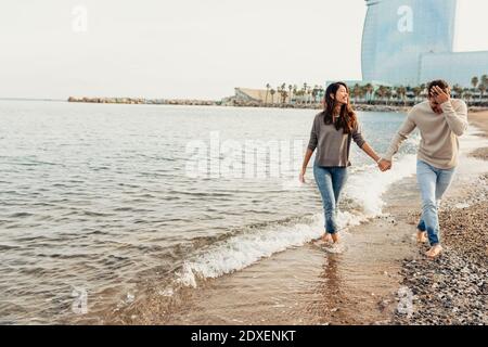 Happy young couple having fun while walking at beach against clear sky Stock Photo