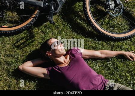 Woman taking a break while lying on grass by electric mountain bike at park Stock Photo