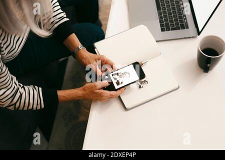 Senior woman taking photo of black and white photograph on book through mobile phone at home Stock Photo