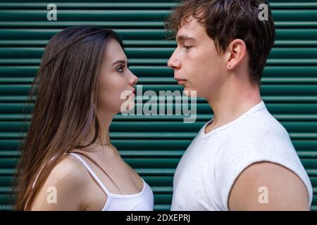Young man and woman looking at each other while standing against shutter Stock Photo