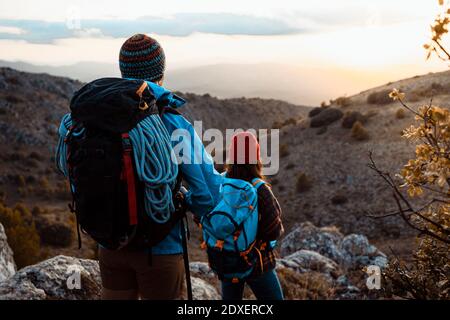 Couple with backpacks looking at view while hiking on mountain during sunset Stock Photo