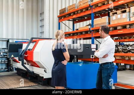 Male colleague and female entrepreneur discussing with while standing in factory Stock Photo