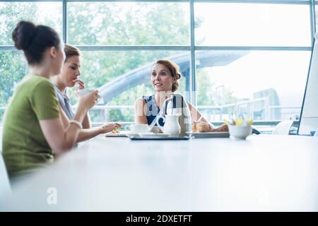 Female professionals discussing in board room while having coffee at office Stock Photo