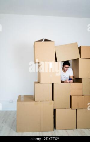 Young man using smart phone while leaning on boxes in new house Stock Photo