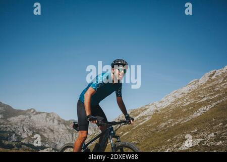 Male cyclist riding mountain bike against sky on sunny day, Picos de Europa National Park, Asturias, Spain Stock Photo