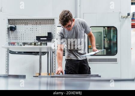 Male engineer holding clipboard while examining machinery in industry Stock Photo