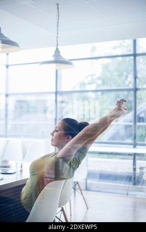 Tired young businesswoman stretching arms while sitting at desk in office Stock Photo