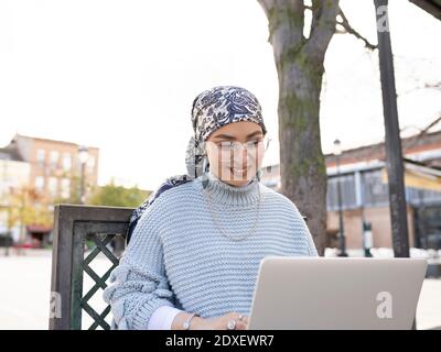 Smiling woman using laptop while sitting outdoors Stock Photo