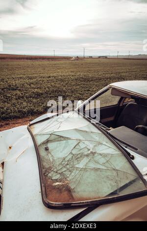 White wrecked car abandoned in middle of field Stock Photo