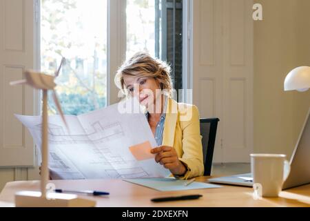 Female engineer analyzing blueprint while sitting in office Stock Photo