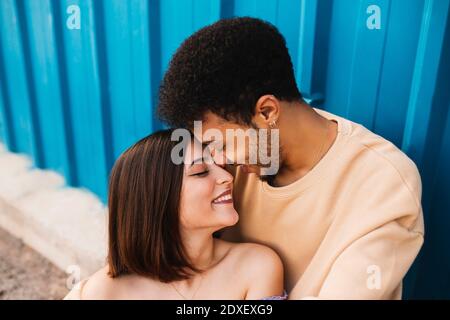 Smiling young couple sitting face to face against blue wall Stock Photo