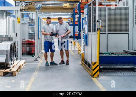 Professional male engineers discussing while standing in industry Stock Photo