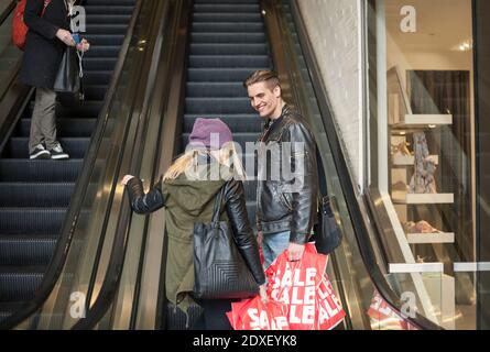Young couple carrying shopping bags while standing on escalator in shopping mall Stock Photo