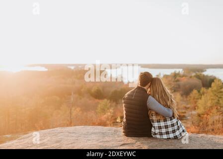 Young couple sitting together on rocky surface admiring setting sun in autumn Stock Photo