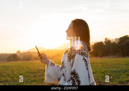 Cheerful young woman using mobile phone during sunset Stock Photo