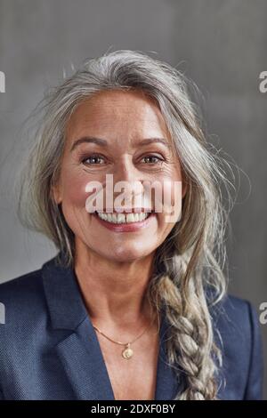 Happy businesswoman with gray hair against wall at home office Stock Photo